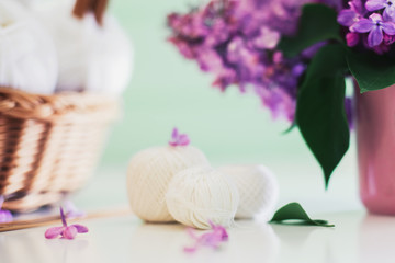 Crochet and knitting. Women's working space. Bouquet of lilac, yarn, crochet hooks on the white dresser in the mint wooden room. Favorite hobby.