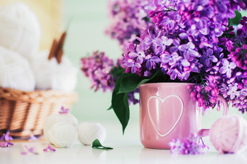 Crochet and knitting. Women's working space. Bouquet of lilac, yarn, crochet hooks on the white dresser in the mint wooden room. Favorite hobby.