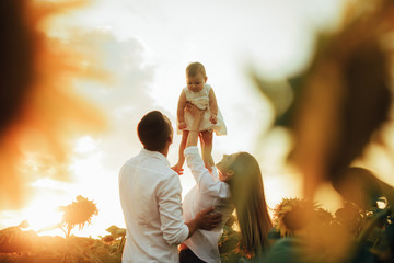 Happy family with baby has a fun and plays in the sunflower field.