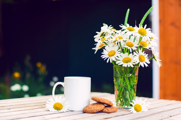 Cup of hot coffee,  biscuits and a bouquet of chamomiles on a rustic wooden background