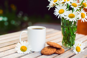 Cup of hot coffee,  biscuits and a bouquet of chamomiles on a rustic wooden background
