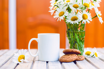 Cup of hot coffee,  biscuits and a bouquet of chamomiles on a rustic wooden background