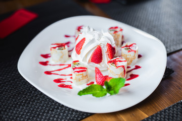 Dessert in a cafe. Dessert of cake with whipped cream, meringue, ice cream, decorated with fresh strawberries and mint. Rolls of dough with jam and cream.