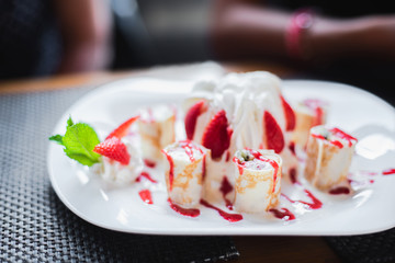 Dessert in a cafe. Dessert of cake with whipped cream, meringue, ice cream, decorated with fresh strawberries and mint. Rolls of dough with jam and cream.