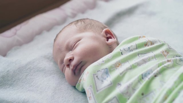 cute baby with adorable cheeks and closed eyes sleeps and moves hands under muslin swaddle close view