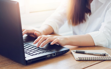 Closeup of hands young asian woman typing on keyboard of laptop to working with notebook and pen on wooden table