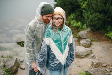 Portrait of young couple  standing and hugging under the rain in park on front of the lake in mountains. Beautiful couple spending time together. Travel concept