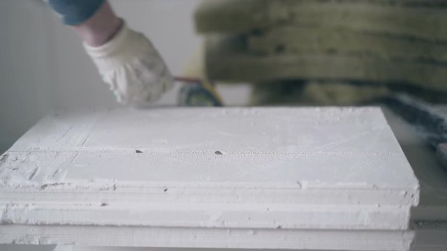 skilled man hands in white gloves and blue sweatshirt measure gypsum plasterboard and ruler with pencil close view