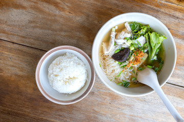 Soup with thin noodle, pock, pock stick, mushroom, vegetable in white bowl near have rice in small bowl on wood table. with copy space for text or design