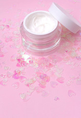 Fototapeta na wymiar Cosmetic cream lotion jar on pink holographic heart confetti sparkles background with copy space.