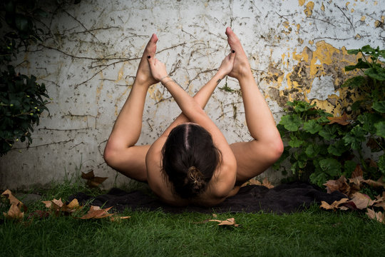 Young nude tattoo girl doing yoga pose on the grass