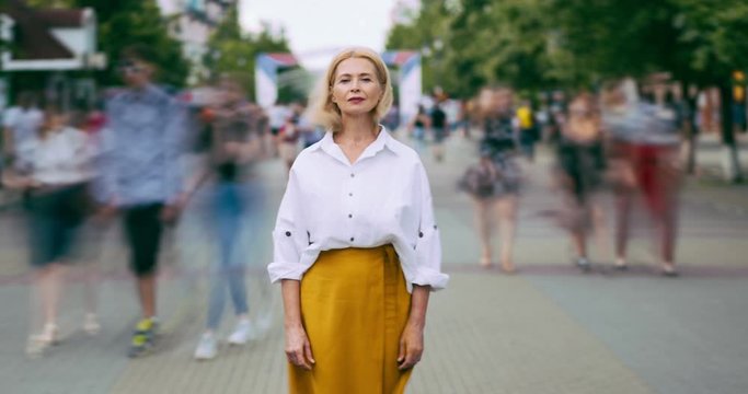 Time lapse portrait of good-looking mature woman in elegant clothing in street standing alone looking at camera with serious face. People, life and summer concept.