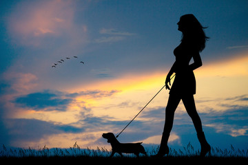woman walks with dog on a leash at sunset
