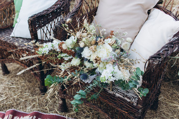 Wedding asymmetrical stylish bouquet with roses on a boho wicker chair.