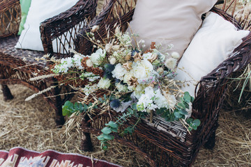 Wedding asymmetrical stylish bouquet with roses on a boho wicker chair.