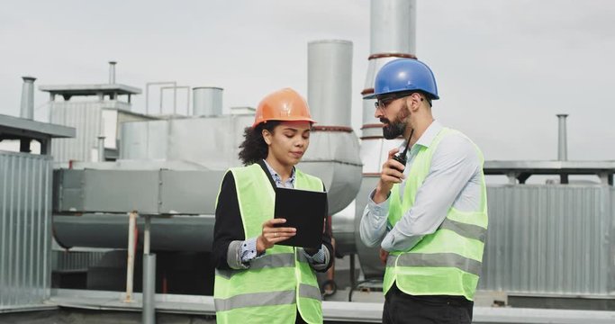 African woman architect explain the plan of construction site to the foreman while holding a tablet foreman explaining using a ration to other workers in a construction site, they wearing helmets