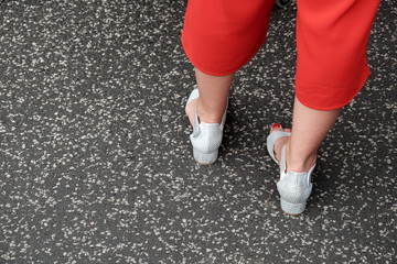 Offene Damenschuhe mit Absatz auf grauem Asphalt und rote Caprihose im Stil der Fünfzigerjahre im...
