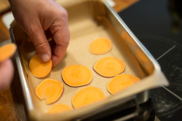 Mann legt dünne Süsskartoffel-Scheiben in einen Bräter, Nahaufnahme mit Hand