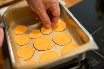 Bratenform mit vielen dünnen Scheiben Süsskartoffel, Hand von einem Mann legt weitere Scheiben dazu, Nahaufnahme
