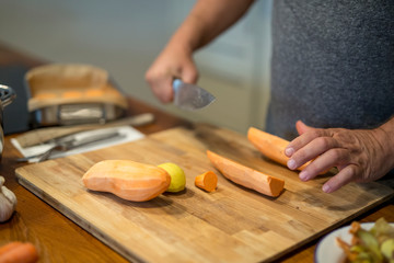 Süsskartoffel mit dem Messer halbiert, Hände eines Mannes, weitere Zutaten, Nahaufnahme