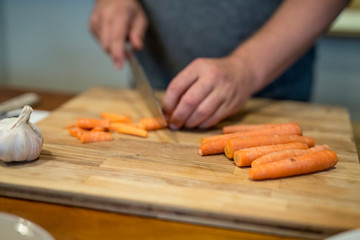 Möhren und Knoblauch auf einem Holz Schneidebrett, Männer Hände schneiden großem Küchenmesser,...