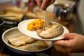 Fischfilet in Butter gebraten auf Teller anrichten, Süsskartoffel Püree, Pfanne und Herd im...
