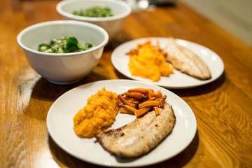 Teller mit Fischfilet, Möhren, Süsskartoffel-Püree, Feldsalat, Schüssel, Holztisch, Nahaufnahme