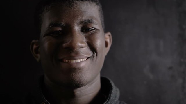 Happy attractive young black african man smiling at camera in the darkness