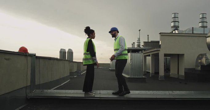 Beautiful couple of architects multiethnic on the rooftop of construction site man make a proposal for his woman they wearing a safety equipment helmets she was very impressed and happy hugging each