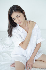 Asian women wear white pajamas in the bedroom. She has pain in the neck area.