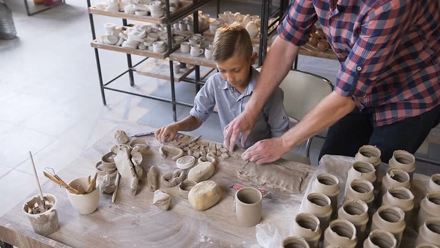 Caucasian caring father helping little son making ceramic vase.
