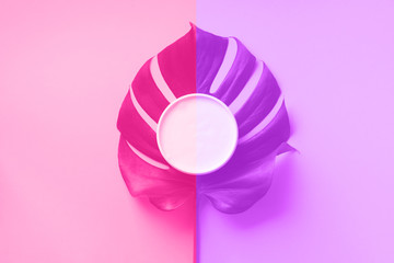 Moisturizing skin care cream on monstera leaf over trendy violet and pink neon color background with copy space. Top view. Flat lay. Cosmetics, beauty, body treatment concept