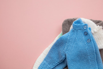 Cute knitted baby clothes layout on a pastel pink background