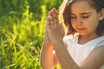 Little Girl closed her eyes, praying in a field during beautiful sunset. Hands folded in prayer...