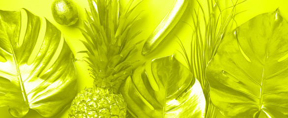 Creative layout. Gold pineapple and golden palm, monstera on trendy yellow neon color background with copy space. Top view. Tropical flat lay. Exotic food concept, crazy trend. Banner