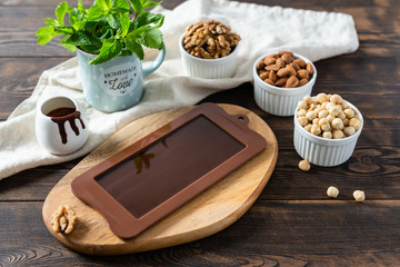 Dark homemade chocolate bar in mold with different nuts on dark wooden table. Healthy food. Handmade sweets