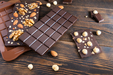 Chocolate bars with nuts and mold on dark wooden background, close up. Homemade chocolate, sweets
