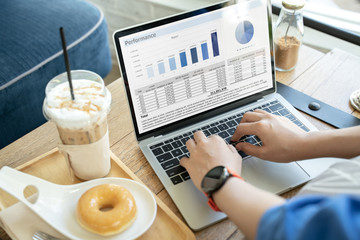Female hands using laptop with business graphs while sitting next to coffee and donut.Financial report with pie chart and data on a laptop with business woman's hands at coffee shop cafe.