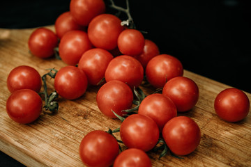 Cherry tomatoes on the vine on rustic wooden board on black background