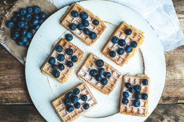 a plate with waffles, dusted with powdered sugar and fresh blueberries
