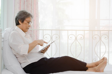 Older women in Asia are playing tablet in the morning.The elderly Asian has white hair, she is resting.