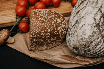 Fresh bread, cherry tomatoes on paper on wooden black background
