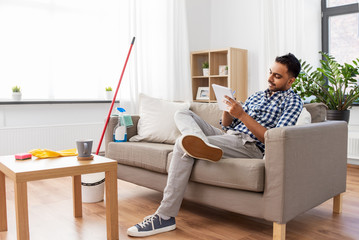 household and time management concept - indian man making to do list in notebook after home cleaning
