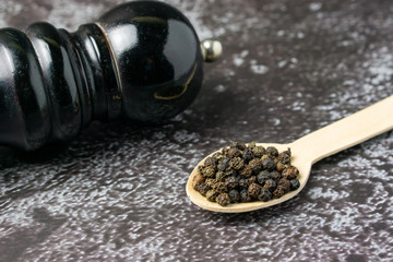 Black pepper on wooden spoon on dark background.