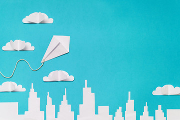 Origami kite in the sky with clouds and city silhouette paper cut banner design.