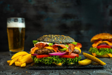 black cheeseburger with baked ham, fresh, colorful vegetables on a dark background