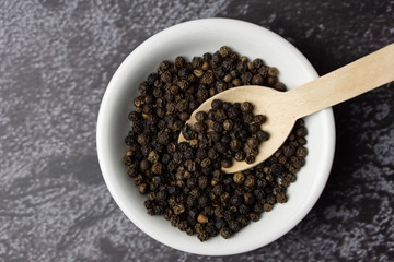 Black pepper in a bowl on dark background.