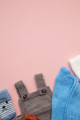 Cute handmade knitted baby clothes layout on a pastel pink background