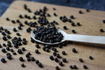 Fototapeta na wymiar Black pepper in wooden spoon on dark background.