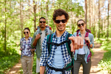 Fototapeta premium travel, tourism, hike and people concept - group of friends with backpacks and man pointing finger to you in forest